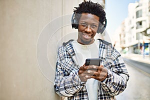 Handsome black man with afro hair wearing headphones and listening to music using smartphone