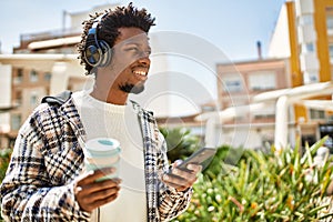 Handsome black man with afro hair wearing headphones listening to music using smartphone