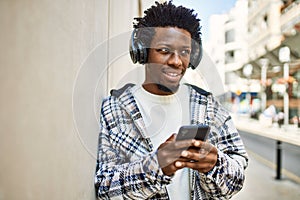 Handsome black man with afro hair wearing headphones and listening to music using smartphone
