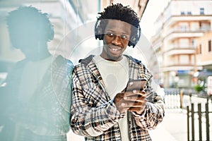 Handsome black man with afro hair wearing headphones and listening to music using smartphone