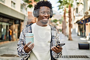 Handsome black man with afro hair wearing headphones listening to music using smartphone