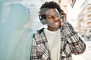 Handsome black man with afro hair wearing headphones smiling happy outdoors