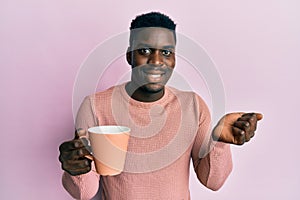 Handsome black man drinking a cup of coffee screaming proud, celebrating victory and success very excited with raised arm