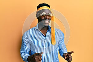 Handsome black man drunk wearing tie over head and sunglasses smiling and looking at the camera pointing with two hands and