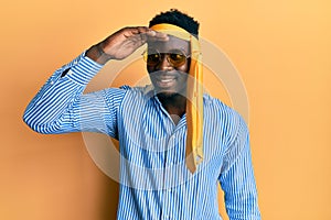 Handsome black man drunk wearing tie over head and sunglasses very happy and smiling looking far away with hand over head