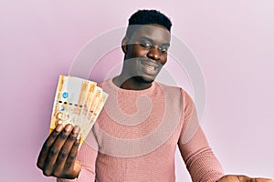 Handsome black man holding 500 philippine peso banknotes celebrating achievement with happy smile and winner expression with