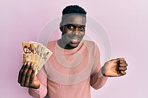 Handsome black man holding 5000 hungarian forint banknotes screaming proud, celebrating victory and success very excited with