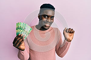 Handsome black man holding south african 10 rand banknotes screaming proud, celebrating victory and success very excited with