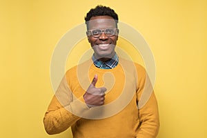 Handsome black man shoing thumb up. Studio shot on yellow wall
