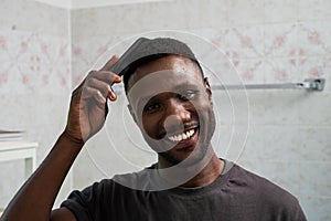 Handsome Black Man Smiling and Combing Hair in Bathroom