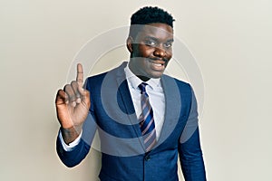 Handsome black man wearing business suit and tie smiling with an idea or question pointing finger up with happy face, number one