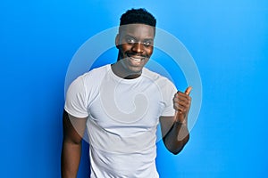 Handsome black man wearing casual white t shirt pointing thumb up to the side smiling happy with open mouth