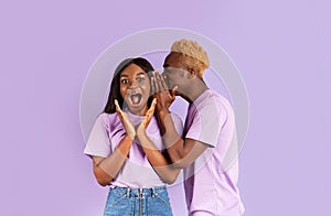 Handsome black man whispering secret or interesting gossip to woman`s ear on color background
