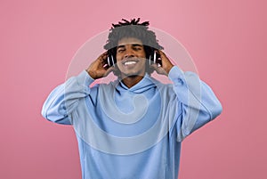 Handsome black teenager in casual clothes listening to music in wireless headphones, relaxing with closed eyes