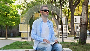 Handsome blinded man reading by touching braille book in park