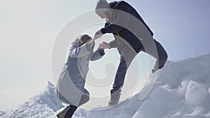 Handsome blond bearded man giving hand to attractive young woman helping her to climb on the ice block. A couple of