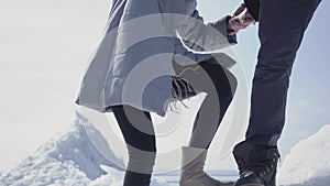 Handsome blond bearded man giving hand to attractive young woman helping her to climb on the ice block. A couple of