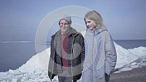 Handsome blond bearded man walking with pretty woman holding hands. Amazing view of a snowy North or South Pole on the