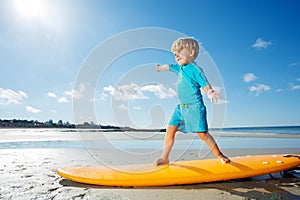 Cute blond boy stand on the surfboard learning balance at beach