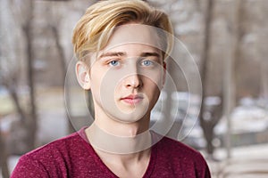 Handsome blond boy teenager in t-shirt poses near window