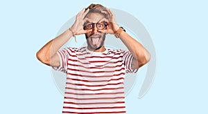 Handsome blond man with beard wearing casual clothes and glasses doing ok gesture like binoculars sticking tongue out, eyes
