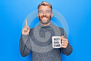 Handsome blond man drinking cup of coffee with best dad ever message over blue background smiling with an idea or question