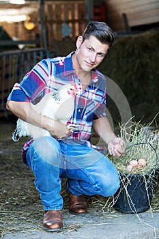 Handsome blond man holding a white chicken with a basket of eggs