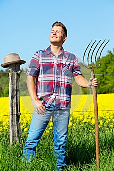 Handsome blond man with pitchfork in front of yellow field