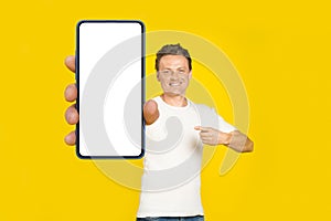 Handsome blond man pointing at giant smartphone with white empty screen, wearing white t-shirt and jeans cellphone