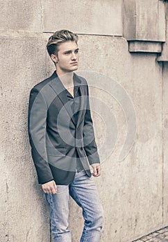 Attractive blue eyed, blond young man leaning against white wall