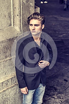 Attractive blue eyed, blond young man leaning against white wall