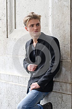 Handsome blond young man leaning against white wall