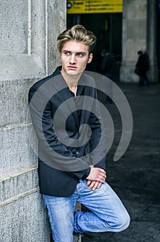 Handsome blond young man leaning against white wall