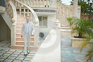 Handsome and blondy groom walking to brides room across terrace.