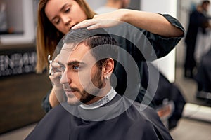 Handsome blue eyed man sitting in barber shop. Hairstylist Hairdresser Woman cutting his hair. Female barber