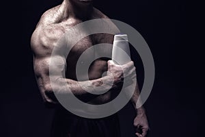 Handsome bodybuilder man with muscular body holds shampoo bottle