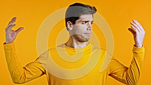 Handsome bored man showing bla-bla-bla gesture with hands and rolling eyes isolated on yellow background. Empty promises