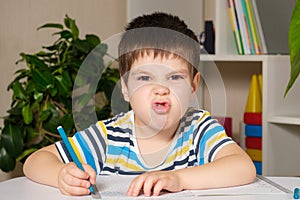 A handsome boy of 4 years old learns to write, looks into the camera and grimaces.
