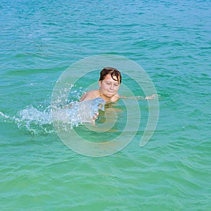 handsome boy enjoys sputtering with his hand in the tropical ocean