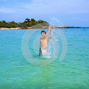 handsome boy enjoys sputtering with his hand in the tropical ocean