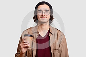 Handsome boy has curly hair, beard wears round transparent glasses, holds coffee to go, has break, communicates with friends, mode