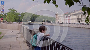 Handsome boy leans his hands on metal fence of Fontanka River, admires city