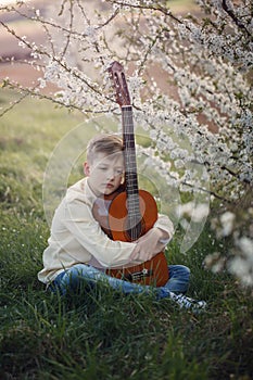Handsome boy making music playing the guitar sitting on the grass in summer day.