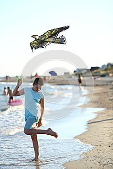 Handsome boy in shorts and a t-shirt teenager launches a kite on the sky on the seashore