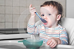 Handsome boy with spoon smiles on blue background. oncept of healthy eating and first feeding of children, food additives,