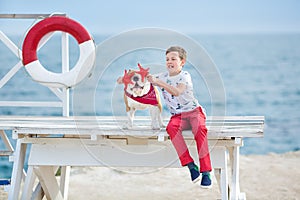 Handsome boy teen happyly spending time together with his friend bulldog on sea side Kid dog holding playing two sea stars close t