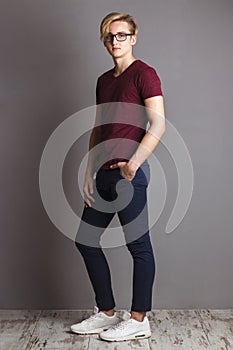 Handsome boy teenager stands near wall in grey studio