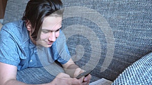 Handsome boy teenager talking on the phone sits on a gray sofa