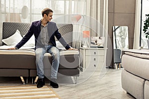 Handsome brown-haired man trying the bed for strength in store