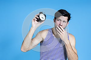 Handsome Brunet Man in Striped Underware During Early Morning Yawing While Having Alarm Clock Close To Ear Against Seamless Blue